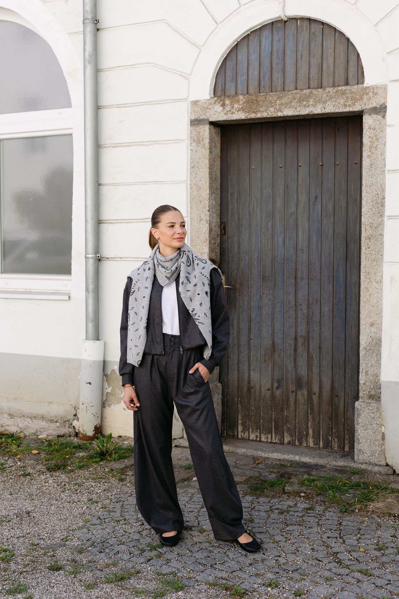 Graues Strick-Set mit Bandana-Schal und weiter Flanellhose vor alter Holztür
